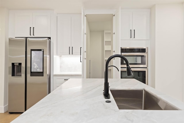 kitchen featuring light stone countertops, a sink, stainless steel appliances, and white cabinets