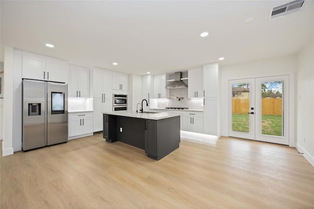 kitchen with visible vents, light wood finished floors, stainless steel appliances, white cabinetry, and wall chimney range hood