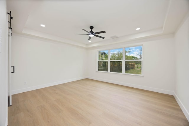 unfurnished room featuring a tray ceiling, baseboards, a barn door, and light wood-style flooring