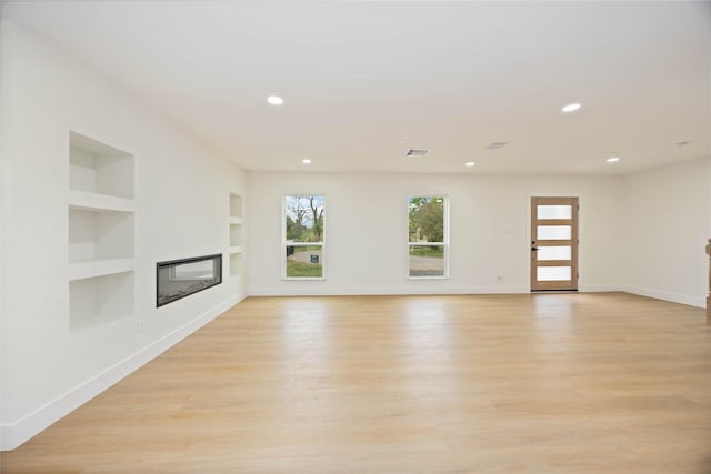unfurnished living room with light wood finished floors, baseboards, built in features, and a glass covered fireplace