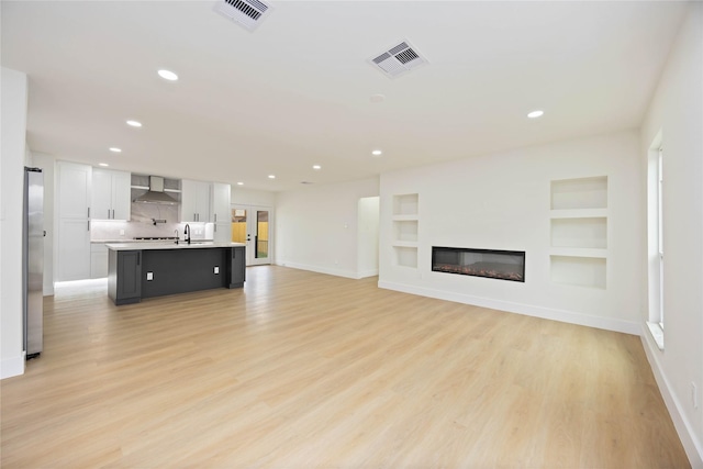 unfurnished living room featuring visible vents, light wood-style floors, and built in shelves