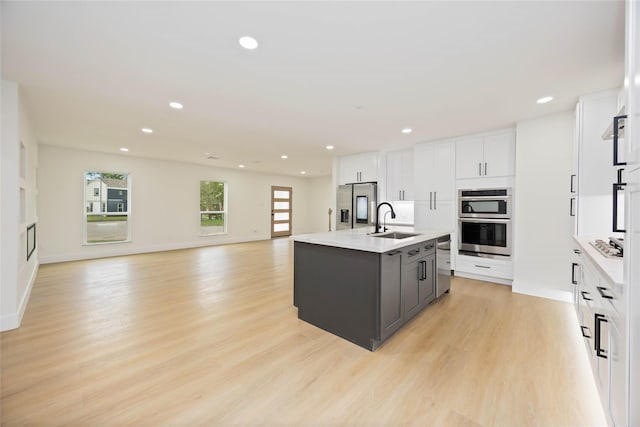 kitchen featuring appliances with stainless steel finishes, white cabinetry, light wood-style floors, and a sink