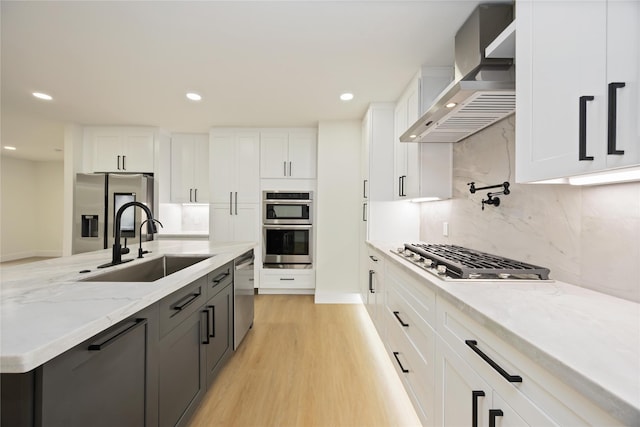 kitchen featuring white cabinets, a sink, wall chimney exhaust hood, and appliances with stainless steel finishes