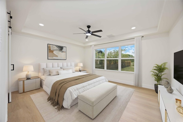bedroom featuring baseboards, light wood-style flooring, and a raised ceiling