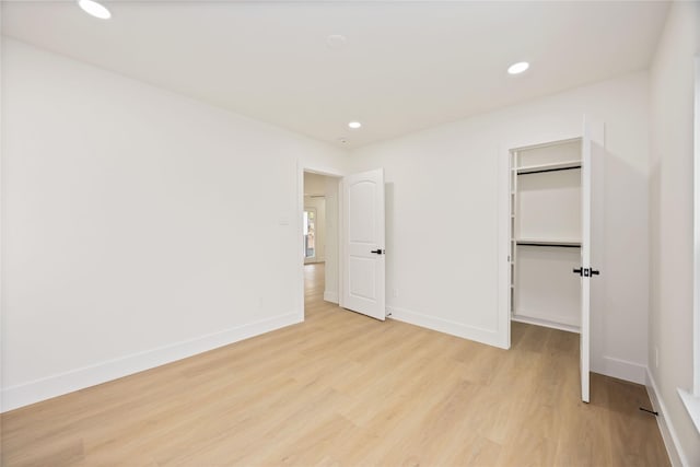 unfurnished bedroom with a closet, a walk in closet, baseboards, light wood-style floors, and recessed lighting