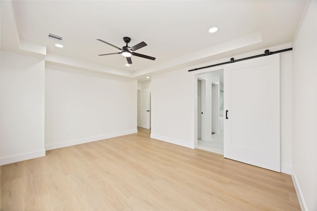 empty room with visible vents, light wood finished floors, baseboards, a ceiling fan, and a tray ceiling