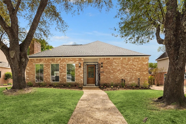 view of front of home with a chimney, brick siding, a front lawn, and roof with shingles