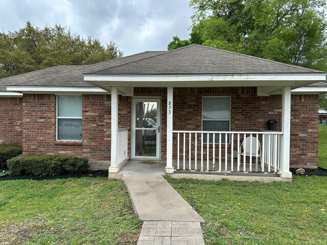 833 E Camp St, La Grange, TX 78945 - view of front of house featuring a front yard, brick siding, a porch, and roof with shingles
