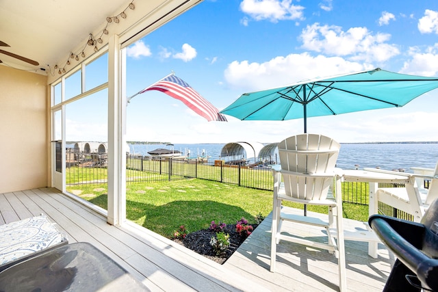deck featuring a water view, fence, a ceiling fan, and a yard