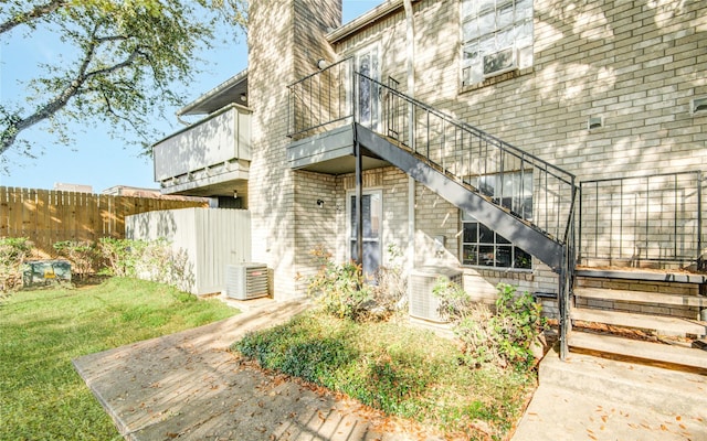 entrance to property with a balcony, fence, a chimney, brick siding, and a lawn