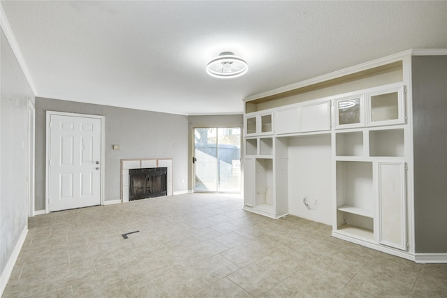 unfurnished living room with built in features, ornamental molding, baseboards, and a tiled fireplace