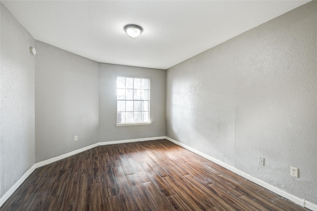 empty room with baseboards, wood finished floors, and a textured wall