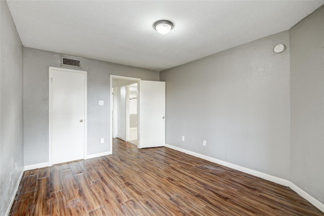 unfurnished bedroom with wood finished floors, a textured ceiling, baseboards, and visible vents