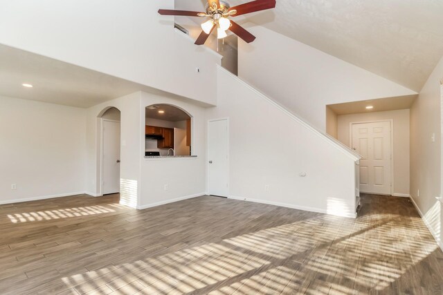 unfurnished living room with high vaulted ceiling, baseboards, wood finished floors, recessed lighting, and a ceiling fan