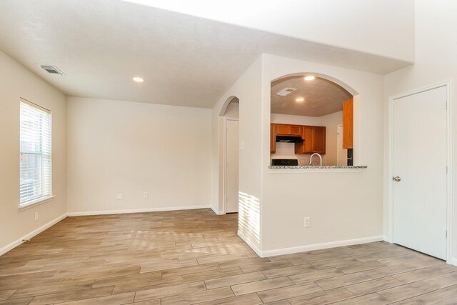 empty room featuring arched walkways, baseboards, visible vents, and light wood finished floors