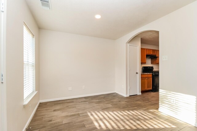 empty room featuring plenty of natural light, visible vents, arched walkways, and light wood-style floors