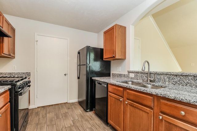 kitchen with wood finish floors, a sink, arched walkways, light stone countertops, and black appliances