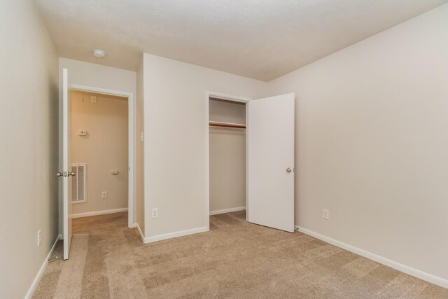 unfurnished bedroom with a closet, baseboards, light colored carpet, and visible vents