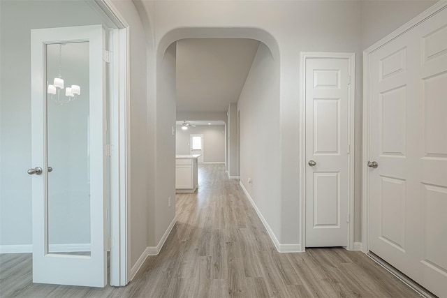 hallway featuring an inviting chandelier, arched walkways, baseboards, and light wood-type flooring