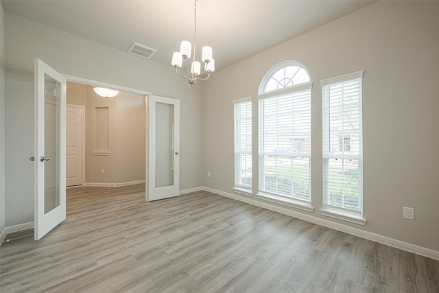 spare room with light wood-style flooring, visible vents, baseboards, an inviting chandelier, and french doors