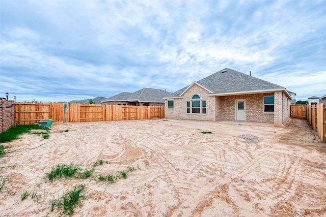 back of house with brick siding, a fenced backyard, and roof with shingles