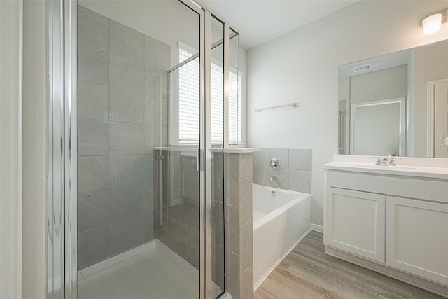 bathroom featuring visible vents, wood finished floors, vanity, a stall shower, and a garden tub