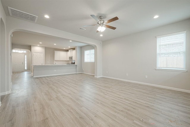 unfurnished living room featuring arched walkways, visible vents, a ceiling fan, and light wood finished floors