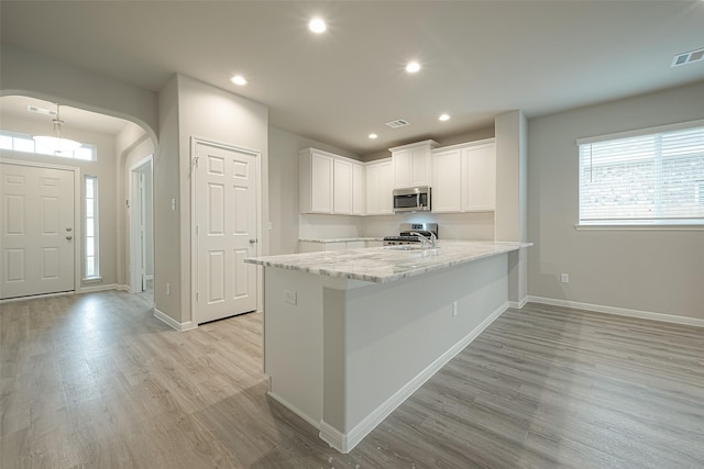 kitchen featuring white cabinets, light wood-style flooring, stainless steel microwave, arched walkways, and a sink