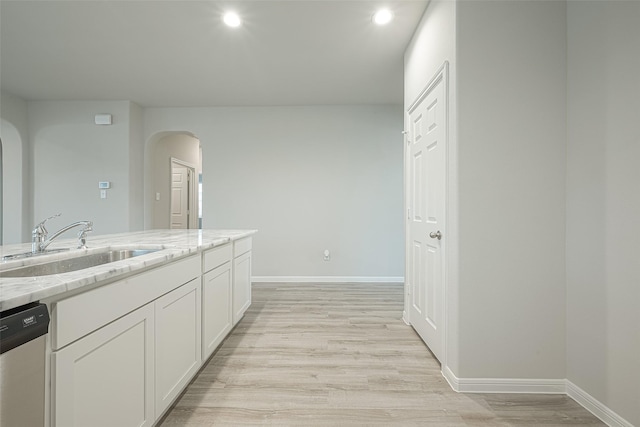 kitchen with a sink, arched walkways, light wood finished floors, and stainless steel dishwasher