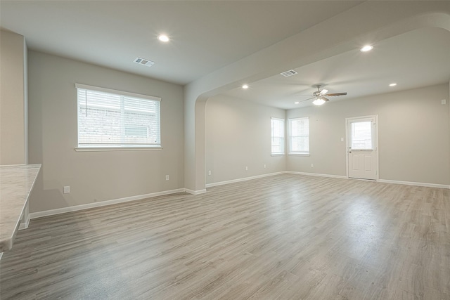 unfurnished room with light wood-type flooring, a ceiling fan, arched walkways, and visible vents