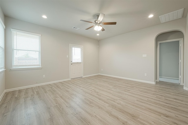 spare room with visible vents, light wood-style flooring, arched walkways, and a ceiling fan