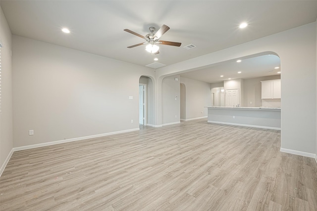 unfurnished living room with baseboards, arched walkways, light wood-style floors, visible vents, and a ceiling fan