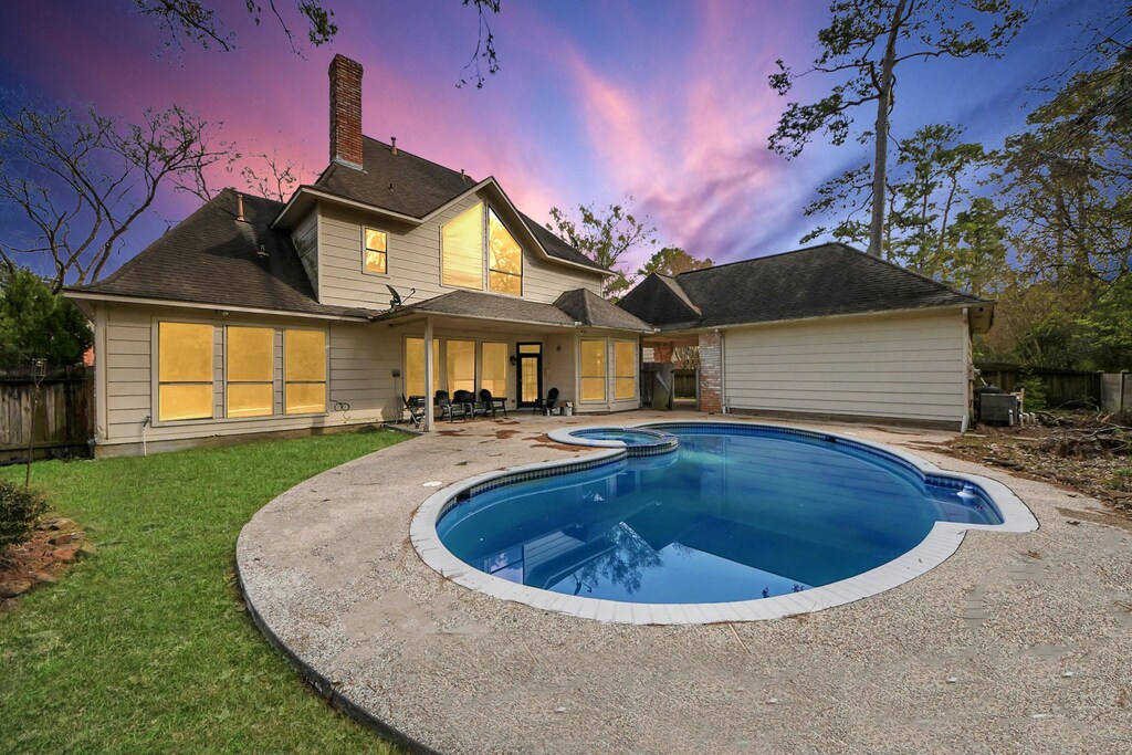 1715 Lofty Maple Trl, Houston, TX 77345 - back of house at dusk with a pool with connected hot tub, a patio area, a chimney, fence, and a lawn