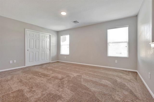 unfurnished bedroom with multiple windows, visible vents, baseboards, and carpet flooring