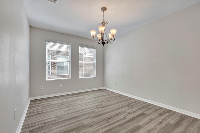 empty room with baseboards, an inviting chandelier, and light wood-style floors