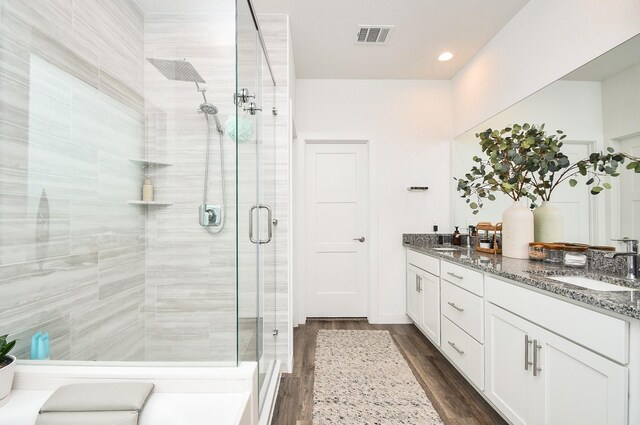 full bath featuring visible vents, a sink, a shower stall, and wood finished floors