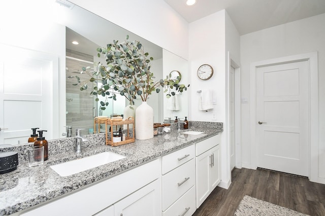 bathroom featuring a stall shower, double vanity, wood finished floors, and a sink