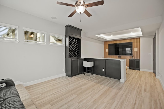 living area featuring baseboards, ceiling fan, light wood finished floors, and a raised ceiling