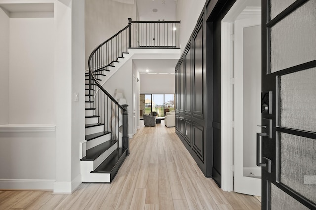 foyer featuring stairs, a high ceiling, light wood-style floors, and baseboards