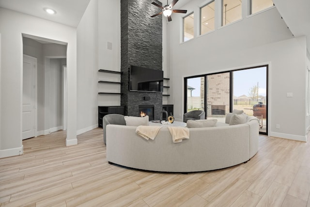 living area featuring baseboards, a large fireplace, wood finished floors, and a ceiling fan