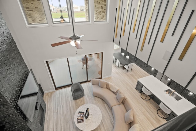 living room featuring baseboards, a towering ceiling, wood finished floors, and a ceiling fan