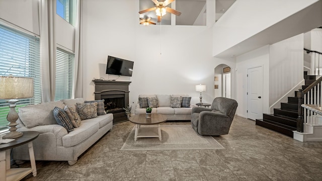living room featuring arched walkways, a high ceiling, a ceiling fan, a fireplace, and stairway