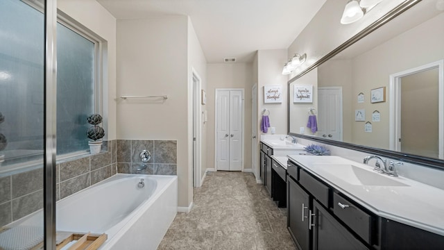 bathroom with a garden tub, double vanity, a sink, and baseboards