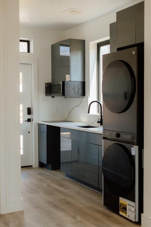 2805 Delano St, Houston, TX 77004 - kitchen featuring stacked washer / dryer, gray cabinetry, light countertops, and light wood finished floors