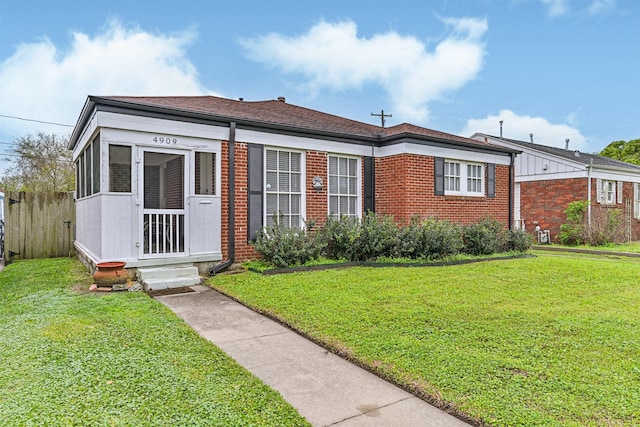 view of front of home with a sunroom, brick siding, and a front yard