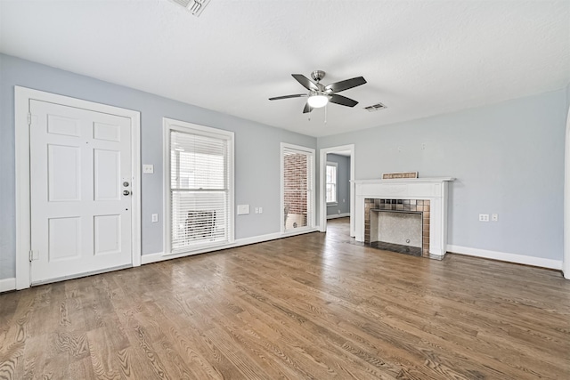 unfurnished living room featuring a ceiling fan, a fireplace, wood finished floors, baseboards, and visible vents