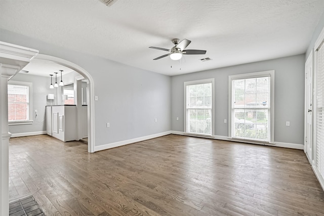 unfurnished living room with a ceiling fan, wood finished floors, baseboards, visible vents, and arched walkways