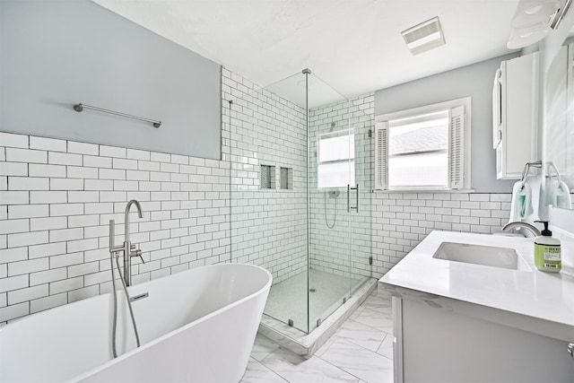bathroom with tile walls, a shower stall, marble finish floor, vanity, and a freestanding bath
