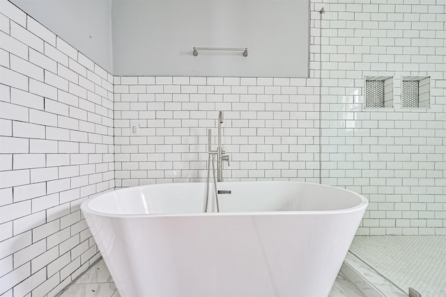 bathroom featuring marble finish floor, a freestanding tub, and tile walls