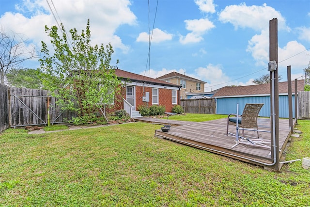 rear view of property with a wooden deck, entry steps, a fenced backyard, brick siding, and a lawn